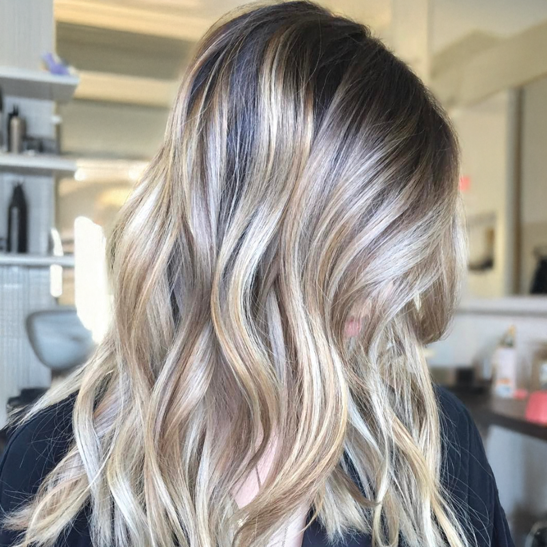 Shadow root balayage with dark roots blending into lighter ends, styled in voluminous waves for a dimensional fall 2025 hair trend.